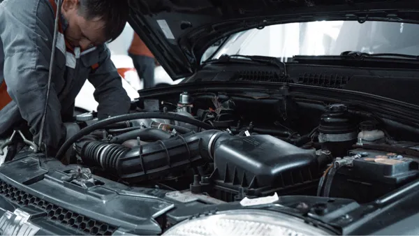 Kaputu açık bir aracın motor bölümünde şarj sistemini kontrol eden teknisyen